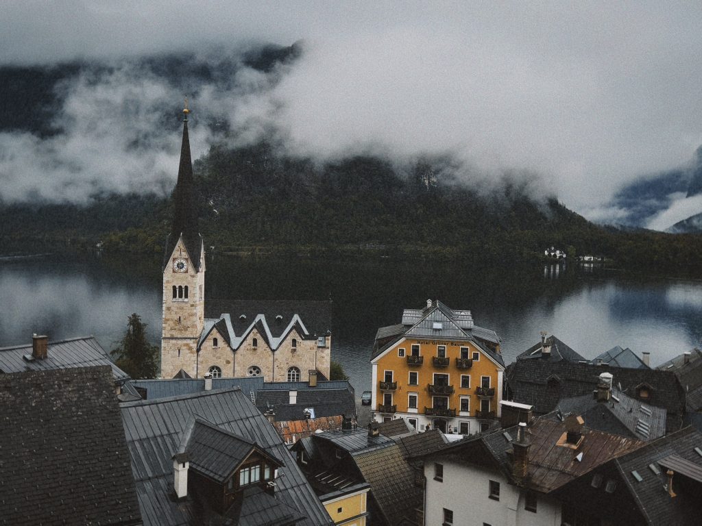 Scenic view of Hallstatt village with iconic church and serene lake surrounded by misty mountains.