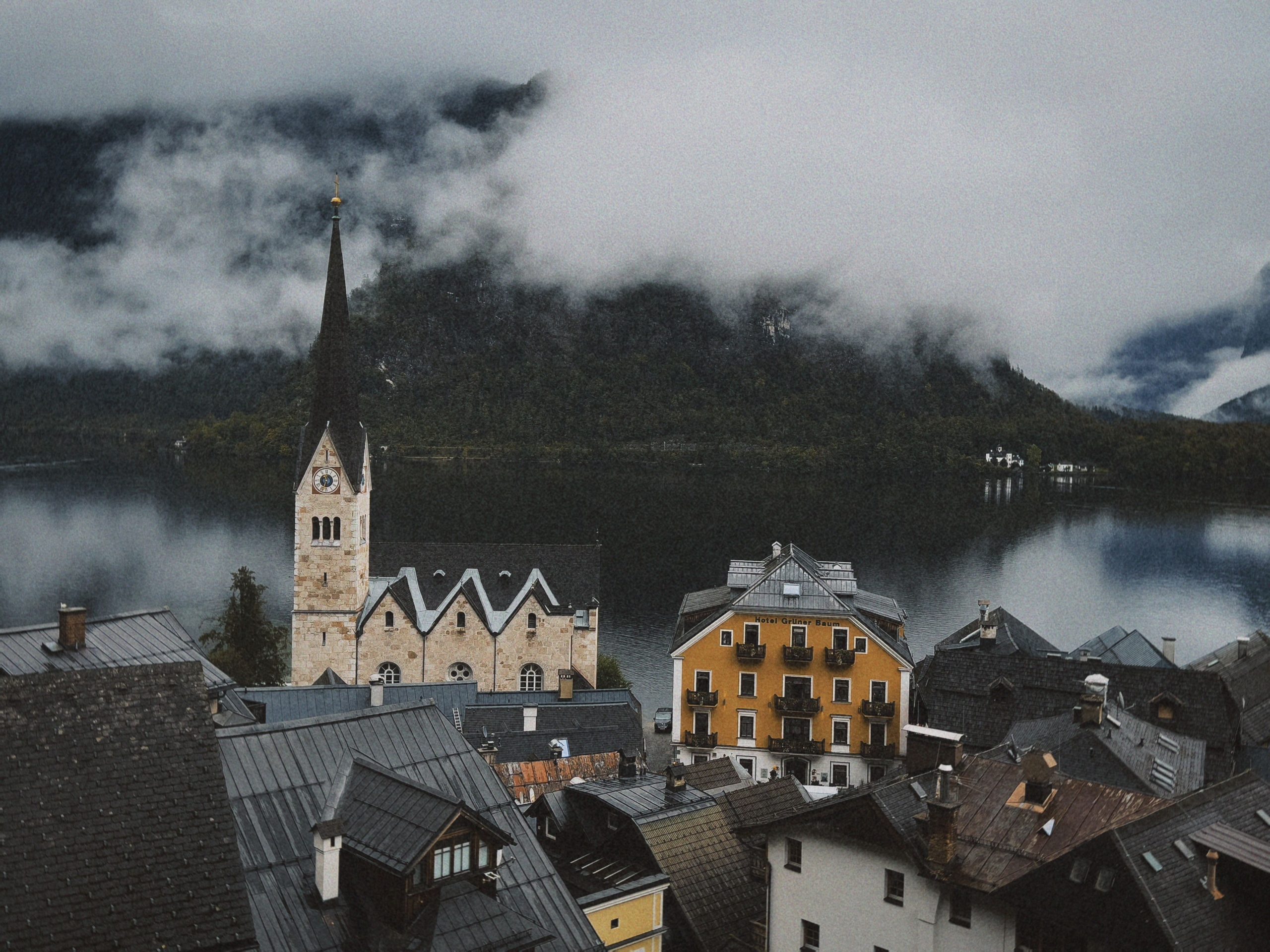 Blog Scenic view of Hallstatt village with iconic church and serene lake surrounded by misty mountains.